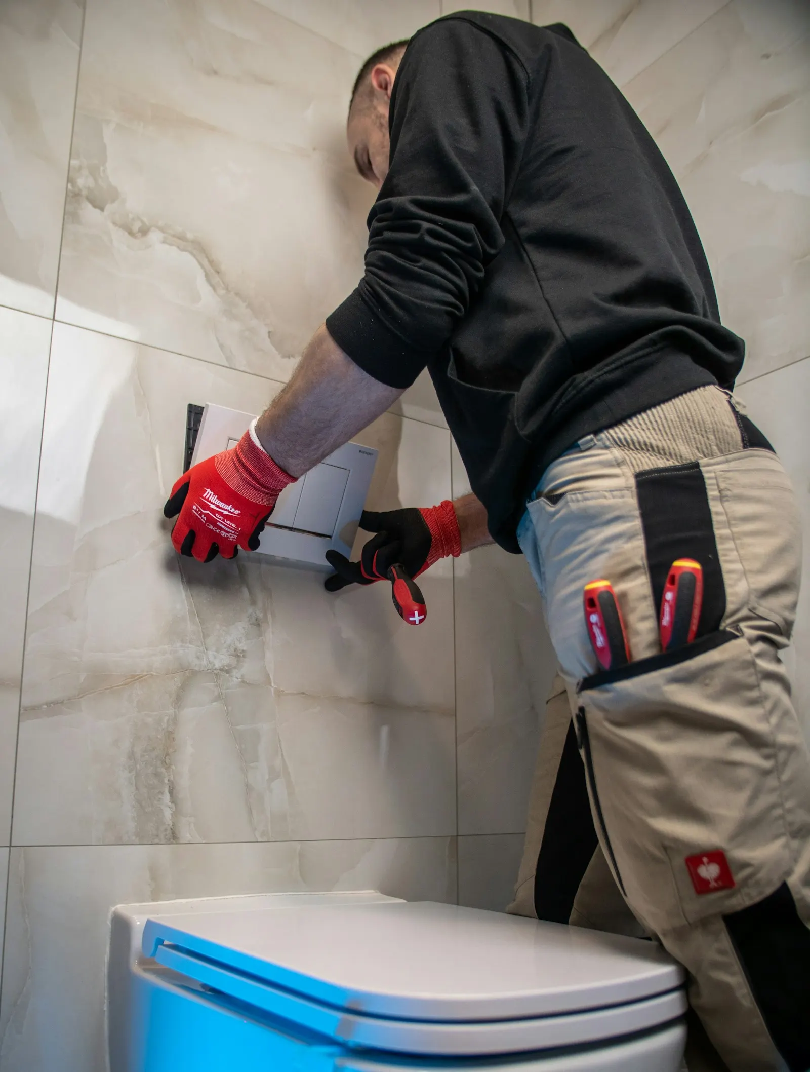 A plumber in red gloves fitting a toilet flush plate